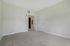 Princeton Westford Apartments | Empty room in an apartment in Westford MA with beige carpet, white walls, and two white doors—one open to a wood-floored hallway. Electrical outlets and a wall vent are also visible. | Wheelchair Accessible Apartments in Westford