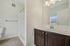 Princeton Westford Apartments | Modern bathroom in an apartment in Westford, MA, featuring a dark wood vanity, white countertop, large mirror, sink, and walk-in shower. Light-colored walls complement the space with a towel bar and a partially visible toilet on the left. | Apartments with Air Conditioning in Westford
