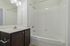 Princeton Westford Apartments | A bathroom in an apartment in Westford, MA features a white bathtub and shower, white tiled walls, a silver shower rod, a white sink with dark wood cabinet, a large mirror, and three lights above the mirror. | Two bedroom apartments in westford