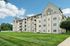 Princeton Westford Apartments | A modern four-story Princeton Westford apartment community in Westford, MA, with beige siding, balconies, and triangular roof features, set beside a large green lawn under a blue sky with scattered clouds. | Pet Friendly Apartments in Westford