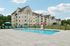 Princeton Westford Apartments | Rectangular salt water pool with lounge chairs, umbrellas, and a lifeguard stand, set in front of the multi-story beige Princeton Westford Apartments, surrounded by green lawn and blue sky. | Apartments with a pool in westford