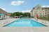 Princeton Westford Apartments | Outdoor salt water pool with clear blue water, surrounded by lounge chairs, umbrellas, and a lifeguard chair. Princeton Westford Apartments and trees are in the background under a partly cloudy sky. | apartments with fitness center in westford ma