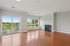 Grandview Apartments | Bright, empty living room at Grandview Apartments in Lowell MA with hardwood floors, a gas fireplace, large windows, and a sliding glass door opening to a balcony overlooking green trees. Light gray walls and white trim. | Apartments with Air Conditioning in Lowell