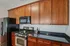 Grandview Apartments | A kitchen at Grandview Apartments in Lowell MA features wooden cabinets, black granite countertops, a stainless steel gas stove, a black microwave, and refrigerator. A wine bottle and glass rest on the counter by the stove. | Apartments with Air Conditioning in Lowell