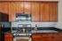 Grandview Apartments | A kitchen at Grandview Apartments in Lowell MA features wooden cabinets, a black granite countertop, stainless steel gas stove, black microwave, refrigerator, and a bottle of wine with two glasses on the counter. | Lowell Waterfront Apartments