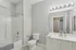 Grandview Apartments | Modern bathroom at Grandview Apartments in Lowell, MA features a white bathtub and shower combo, white toilet, spacious vanity with large mirror, multi-bulb lighting, light gray walls, and tiled floors. | Pet Friendly Apartments in Lowell