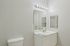 Grandview Apartments | A clean, modern bathroom at Grandview Apartments in Lowell, MA features white walls, a white toilet, and a sleek vanity with a large mirror. Bright vanity lights shine above, with soap and a hand towel neatly placed on the counter. | Apartments with Washer & Dryer in Lowell