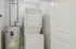 Grandview Apartments | A laundry nook at Grandview Apartments in Lowell, MA features a stacked white washer and dryer next to a water heater against light gray walls, partially enclosed by an open white door. | Apartments with Washer & Dryer in Lowell | Apartments with Balcony in Lowell