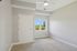Grandview Apartments | A secondary bedroom at Grandview Apartments in Lowell MA features beige carpet, light gray walls, a closed white door, a window with tree views, and a ceiling fan with a light. | Apartments with Air Conditioning in Lowell