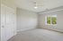 Grandview Apartments | Empty bedroom at Grandview Apartments in Lowell, MA, featuring light gray walls, beige carpet, a white ceiling fan, a closed white door, and a window overlooking green trees under a clear sky. | Pet Friendly Apartments in Lowell