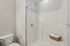 Grandview Apartments | A bathroom at Grandview Apartments in Lowell, MA features a white toilet, wall-mounted toilet paper holder, and a walk-in shower with a built-in corner seat and a basket holding towels on a ledge. | Lowell Waterfront Apartments