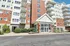 Grandview Apartments | Grandview Apartments in Lowell, MA is a multi-story building with red brick and white siding, featuring balconies, large windows, and a main entrance with a glass door and peaked roof. Shrubs and flowers line the front walkway. | Lowell Waterfront Apartments