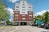 Grandview Apartments | A multi-story apartment building with red brick and white siding, balconies on each floor, and a drive-through passage at the ground level—Grandview Apartments in Lowell MA is surrounded by parked cars and trees under a blue sky with clouds. | Apartments with Washer & Dryer in Lowell
