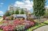 Grandview Apartments | A stone sign reading Grandview Apartment Homes stands amid vibrant pink and white flowers, with a multi-story building and tall green trees in the background under a blue sky at Grandview Apartments in Lowell MA. | Wheelchair Accessible Apartments in Lowell