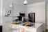 Modern kitchen at The Charley Apartments in Allston MA features white cabinets, stainless steel appliances, a peninsula with beige chairs set for dining, stylish pendant lights above, and abstract art adorning the walls. | The Charley | Apartment in Allston, MA