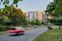 Cars drive along a curved road lined with trees and grass, The Charley Apartments in Allston MA rise in the background on a sunny day. | The Charley | Apartment in Allston, MA