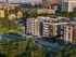 A cityscape shows The Charley Apartments in Allston MA, with modern buildings, a tree-lined street filled with cars, and older architecture in the background, all bathed in late afternoon sunlight. | The Charley | Apartment in Allston, MA