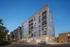 Modern six-story apartment building, The Charley Apartments in Allston MA, features balconies, illuminated windows, and street lamps at dusk. Several parked cars line the quiet street, with neighboring buildings visible in the background. | The Charley | Apartment in Allston, MA