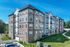 The James Apartments in Haverhill MA is a modern, four-story building with stone and siding exterior, large windows, and balconies, nestled among green grass, trees, and a clear blue sky. | The James | Apartment in Haverhill, MA
