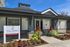 Modern apartment leasing office exterior in Haverhill MA, featuring gray siding, large windows, and a peaked roof. A sign out front reads The James Apartments Leasing Office, with colorful flowers and neatly trimmed bushes lining the walkway. |The James | Apartment in Haverhill, MA