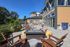 Outdoor patio at The James Apartments in Haverhill, MA features lounge chairs around a modern fire pit, surrounded by tables, potted plants, and a giant Connect Four game beside a tan and green building under a clear blue sky. | The James | Apartment in Haverhill, MA