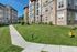 The James Apartments in Haverhill MA features a modern beige and stone exterior, green lawns, small shrubs, a yellow fire hydrant, and a curved sidewalk under a clear blue sky. | The James | Apartment in Haverhill, MA