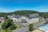 The James Apartments | Aerial view of The James Apartments in Haverhill MA, a modern complex nestled among trees, with a main road and parking lots nearby, set against a forested hill and clear blue sky. | The James | Apartment in Haverhill, MA
