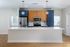 Modern kitchen at The James Apartments in Haverhill MA, featuring a large white island, stainless steel appliances, wood and blue cabinetry, globe pendant lights, light wood flooring, and windows on either side. | The James | Apartment in, Haverhill MA