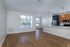 Modern, unfurnished open-plan living space at The James Apartments in Haverhill MA, featuring light wood flooring, large windows, and a kitchen with blue and wood cabinetry, stainless steel appliances, and white countertops.  | The James | Apartment in, Haverhill MA