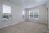 A bright, empty room at The James Apartments in Haverhill, MA features beige carpet, white walls, and three large windows with white blinds letting in natural light. A small doorway is to the right.  | The James | Apartment in, Haverhill MA