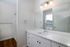 A modern bathroom at The James Apartments in Haverhill, MA features a white vanity, large mirror, three-light fixture, chrome faucet, wood flooring, and a walk-in shower with white tiles illuminated by natural light.  | The James | Apartment in, Haverhill MA