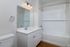 Modern bathroom at The James Apartments in Haverhill, MA, featuring a white vanity, rectangular mirror, three-light fixture, towel ring, toilet, and a bathtub with white subway tile and curved shower curtain rod. Wood-style flooring adds warmth.  | The James | Apartment in, Haverhill MA