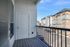 A modern apartment balcony at The James Apartments in Haverhill, MA, features gray flooring, a white door, metal railing, and a view of the parking lot and multi-story buildings on a sunny day  | The James | Apartment in, Haverhill MA