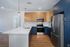 Modern kitchen at The James Apartments in Haverhill MA features stainless steel appliances, blue lower cabinets, wooden uppers, white quartz countertops, tile backsplash, pendant lights over a peninsula island, and light wood flooring throughout.  | The James | Apartment in, Haverhill MA
