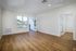 A bright, empty room at The James Apartments in Haverhill MA features light wood flooring, white walls, a large window, a glass door to the balcony, and another door with frosted glass panels leading to a separate space.  | The James | Apartment in, Haverhill MA