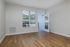 Bright, empty room at The James Apartments in Haverhill MA with light-colored walls, wood flooring, a large window with blinds, and an open door leading to a balcony with black railing and green outdoor view.  | The James | Apartment in, Haverhill MA