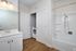 Modern bathroom at The James Apartments in Haverhill MA, featuring a white vanity, large mirror, bathtub with shower, and wood flooring. An open door reveals a washer and dryer in a convenient closet.  | The James | Apartment in, Haverhill MA