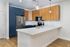 Modern kitchen at The James Apartments in Haverhill MA, featuring white countertops, wood and blue cabinets, stainless steel appliances, built-in microwave, pendant lights over the island, light wood flooring, and a tiled backsplash. | The James | Apartment in, Haverhill MA