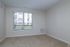 Empty room at The James Apartments in Haverhill, MA, featuring beige carpet, white baseboards, light walls, and a large window with blinds that fill the space with natural light. Apartment buildings are visible outside the window.  | The James | Apartment in, Haverhill MA