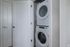 A stacked white washer and dryer set is installed in a small laundry nook at The James Apartments, Haverhill MA, with white walls and an open door. Another closed door is visible to the left.  | The James | Apartment in, Haverhill MA