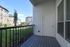 A modern apartment patio at The James Apartments in Haverhill, MA features gray decking, a black railing, and a white door. The view overlooks grass, landscaping, and several multi-story apartment buildings under a blue sky.  | The James | Apartment in, Haverhill MA