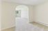 Princeton Place Apartments | A bright, empty room at Princeton Place Apartments in Worcester MA features light beige carpet, white walls, and an arched doorway. A sliding glass door in the background opens to a patio and grassy area outside. | Apartments with Washer & Dryer in Worcester