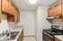 Princeton Place Apartments | A modern galley kitchen at Princeton Place Apartments in Worcester, MA, features wooden cabinets, light marbled countertops, a stainless-steel sink, four-burner electric stove, oven, vent hood, all under a bright ceiling light. | Worcester Apartments with Pickleball Court