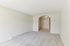 Princeton Place Apartments | Empty room at Princeton Place Apartments in Worcester MA, featuring light-colored carpet, off-white walls, a large archway, baseboard heater, and a closed closet with double doors under a ceiling light. | Wheelchair Accessible Apartments in Worcester