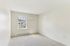 Princeton Place Apartments | A small, empty room with beige carpet, white walls, and a window letting in natural light at Princeton Place Apartments in Worcester MA. Enjoy a baseboard heater under the window and views of parked cars and greenery outside. | Apartments with EV Charging in Worcester