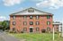 Princeton Place Apartments | Princeton Place Apartments is a three-story red brick building with white trim and a peaked roof, featuring several windows and surrounded by green lawns and shrubs in Worcester MA on a sunny day with blue sky and clouds. | Worcester Apartments with Virtual Tours