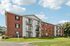 Princeton Place Apartments | Princeton Place Apartments in Worcester, MA is a three-story brick and white-sided building with balconies and window air conditioners, set against a blue sky with clouds, surrounded by green grass and a sidewalk. | Worcester Apartments with Virtual Tours