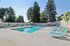 Pheasant Run Apartments | A modern clubhouse with large windows and brown roof stands behind an outdoor swimming pool at Pheasant Run Apartments in Nashua, NH, surrounded by turquoise lounge chairs and a white fence on a sunny day. | Apartments with Air Conditioning in Nashua