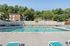 Pheasant Run Apartments | Outdoor swimming pool surrounded by lounge chairs and tables at Pheasant Run Apartments, next to the leasing office/clubhouse with large windows and brown roof in Nashua NH, under a clear blue sky. | Nashua Apartments with Pickleball Court