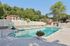 Pheasant Run Apartments | A clear outdoor swimming pool at Pheasant Run Apartments in Nashua, NH, is surrounded by lounge chairs and tables, with a fence and trees in the background next to a building under a sunny sky. | Nashua Apartments with Virtual Tours